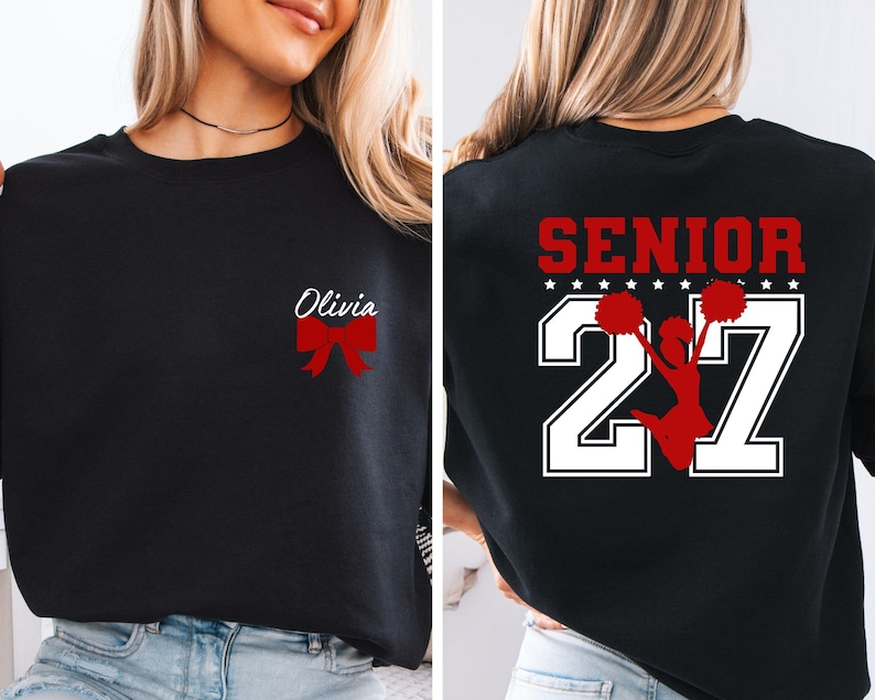 May include: A black sweatshirt featuring a red bow and the name Olivia on the front left chest. The back displays the word SENIOR in red, the number 27 in large white block font, and a red silhouette of a cheerleader holding pom-poms.