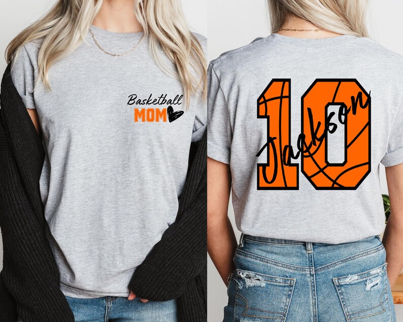 Peut inclure: T-shirt gris avec le texte "Basketball Mom" et un c&oelig;ur noir sur le devant. Le dos du t-shirt a un grand ballon de basket orange avec le num&eacute;ro 10 et le nom "Jackson" &eacute;crit &agrave; l'int&eacute;rieur.