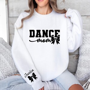 Pu&ograve; includere: Felpa bianca con il testo "Dance Mom" e un fiocco nero. La manica ha il nome "Jessica" e un fiocco nero.