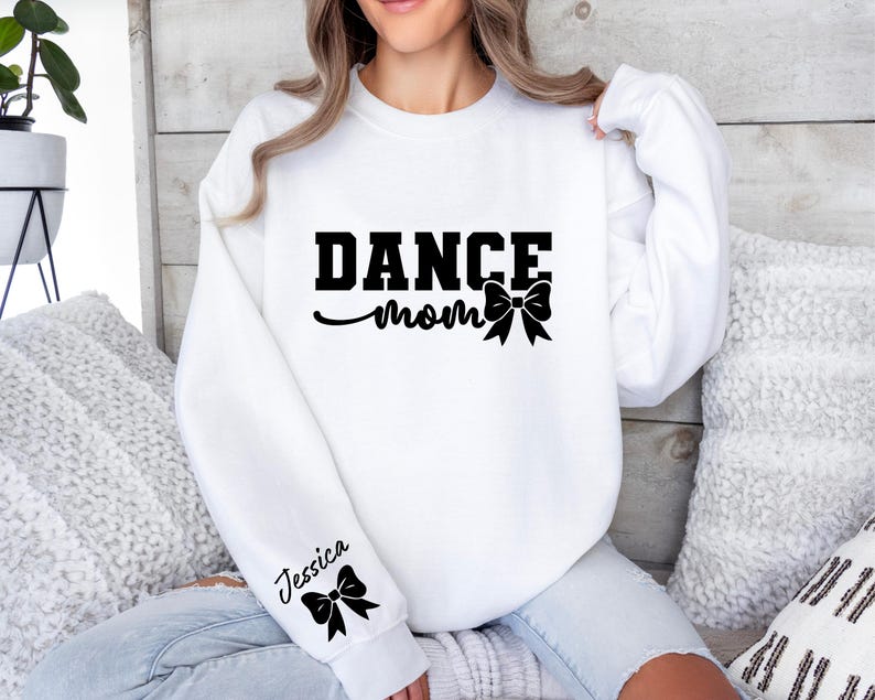 Pu&ograve; includere: Felpa bianca con il testo "Dance Mom" e un fiocco nero. La manica ha il nome "Jessica" e un fiocco nero.