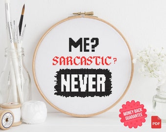 Op de afbeelding: Een witte borduurring met zwarte en rode tekst die "ME? SARCASTIC? NEVER" luidt. De ring staat op een wit oppervlak met een witte bol wol en een spoel garen.