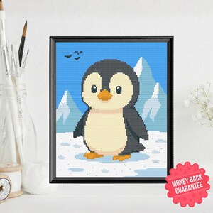 May include: Framed cross-stitch art featuring a cute penguin in a snowy landscape with mountains and birds against a blue sky. The penguin has a black and white body with a yellow beak and feet. The frame is black.