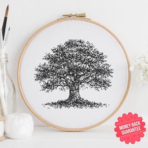 May include: A black and white cross-stitch of a tree in a wooden embroidery hoop. The tree has a detailed, pixelated design. The background is white. The image includes paintbrushes in a glass bottle, a spool of thread, and a red sticker that says "Money Back Guarantee".