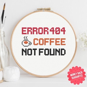 May include: A cross-stitch hoop with the text "ERROR 404 COFFEE NOT FOUND" in red, orange, and black. The design includes a pixelated coffee cup. The hoop is displayed on a white surface.
