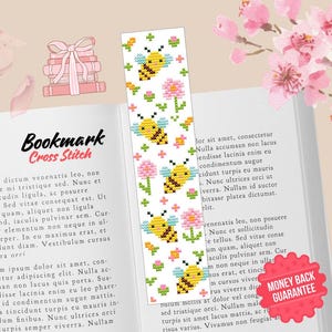 May include: White bookmark with a cross-stitch design featuring yellow bees and pink flowers. The bookmark is on an open book with the words "Bookmark Cross Stitch" at the top. Pink flower petals are scattered around.