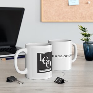 May include: Two white ceramic mugs. One mug features a black square with the letters "EGO" and the word "ERRORGANTONE" in white. The other mug has the phrase "as a me complex" printed on it.