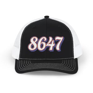 May include: Black and white trucker hat with the number "8647" embroidered in white with blue and orange accents. The hat has a curved brim and a mesh back.