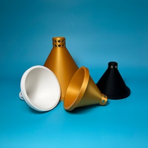 Pode incluir: Três recipientes em forma de funil de tamanhos diferentes. Um é dourado, outro é branco e outro é preto.