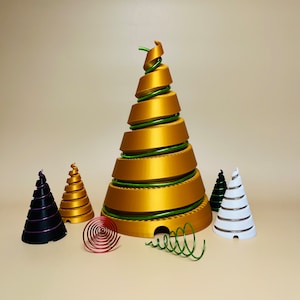 Può includere: Un ornamento per albero di Natale dorato a spirale con accenti di filo verde. Ci sono quattro ornamenti più piccoli in nero, bianco e rosso.