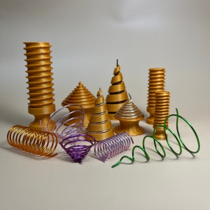 Può includere: Una collezione di oggetti stampati in 3D di colore dorato a forma di spirale, alcuni con accenti argentati, e molle metalliche colorate.