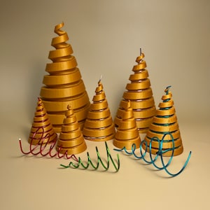 Op de afbeelding: Vijf gouden spiraalvormige kerstboomversieringen in verschillende maten, met drie rode, groene en blauwe draadversieringen ervoor.