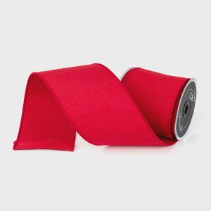 Puede incluir: Un rollo de cinta roja brillante con una superficie texturizada. La cinta ancha parece estar hecha de un material similar al sat&eacute;n. El carrete es visible en el lado derecho, con una etiqueta negra y plateada.
