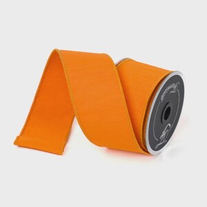 Puede incluir: Un carrete de cinta naranja brillante con una superficie texturizada. La cinta est&aacute; enrollada en un carrete negro con texto blanco. Adecuado para manualidades, envolver regalos o decoraci&oacute;n.