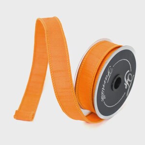 Puede incluir: Un carrete de cinta naranja con una apariencia texturizada. La cinta est&aacute; desenrollada, revelando su color y textura. El carrete es negro y tiene el texto "Farrisilk" en cursiva.