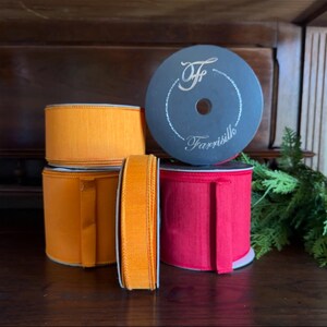 Puede incluir: Un surtido de carretes de cinta colorida. La imagen presenta carretes naranjas, rojos y uno gris oscuro con el texto "Farrisilk". La cinta naranja es de un tono vibrante, mientras que la cinta roja ofrece un contraste audaz. Los carretes est&aacute;n dispuestos sobre una superficie de madera oscura.