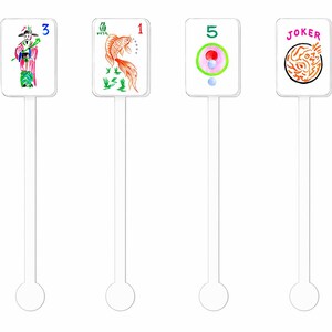 May include: Four clear plastic drink stirrers with rectangular tops featuring colorful illustrations. The illustrations include a figure in traditional garb, a koi fish, a circle design, and the word "JOKER". Each stirrer has a long stem and a circular base.