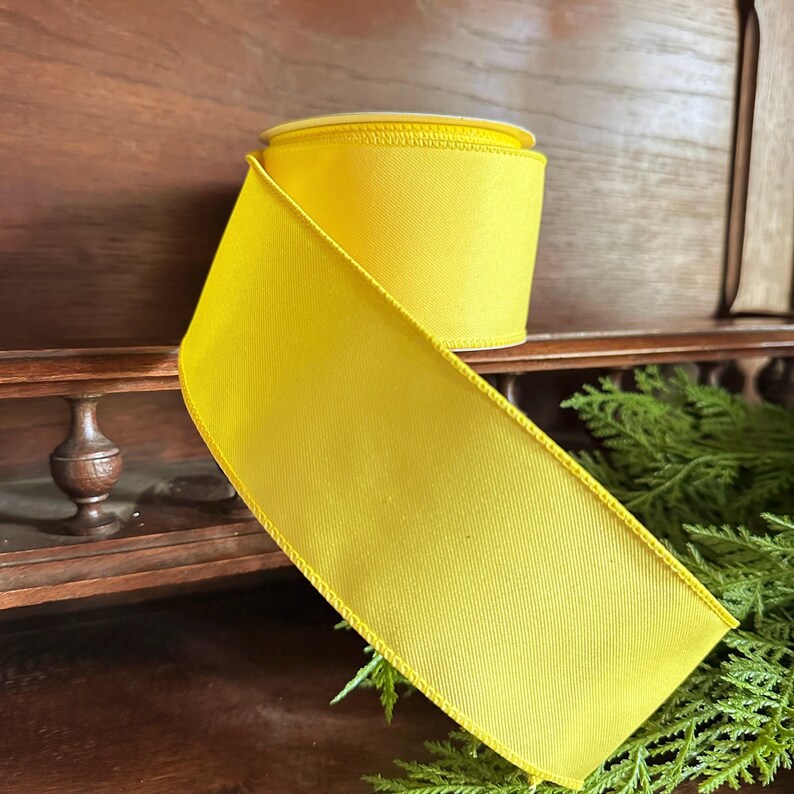 May include: A roll of bright yellow satin ribbon with a wired edge. The ribbon is on a wooden surface.