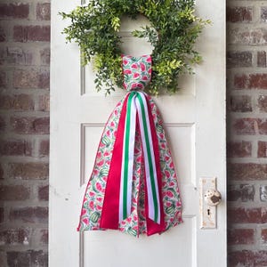 May include: A watermelon-patterned ribbon bow with red, green, and white stripes, tied to a wreath on a white door.