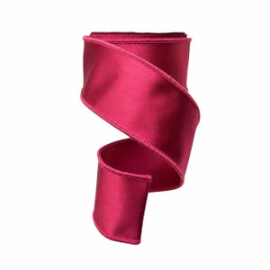 May include: A deep magenta satin ribbon with a smooth, reflective surface and finished stitched edges. The ribbon is coiled into a loose, open spiral shape, showcasing the vibrant, solid color and the consistent texture of the fabric material.