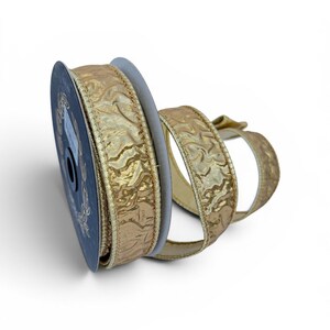May include: A spool of gold ribbon with a textured, crinkled surface and metallic sheen. The ribbon is wound around a dark circular core and features finished edges, with a portion of the gold fabric extending outward in a loose, curved loop.