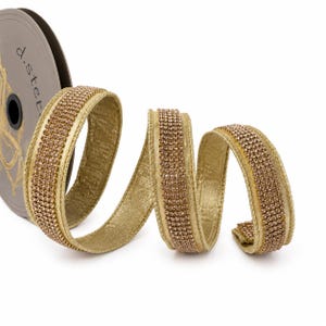 May include: A gold-colored ribbon on a spool, featuring a central strip of small, sparkling rhinestones. The ribbon has a metallic sheen and is coiled to show its texture and flexibility. The spool is labeled with the text d.stevens.