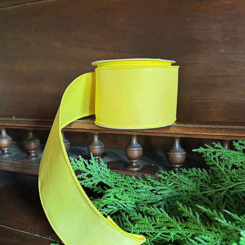 May include: A roll of bright yellow satin ribbon. The ribbon is wound around a spool and is ready to be used for crafting or decorating.