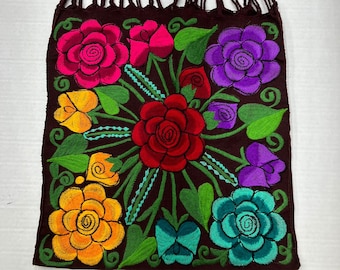 May include: A brown fabric tote bag with a floral design. The bag has a woven strap and is decorated with colorful embroidered flowers, including red, pink, purple, yellow, and blue.