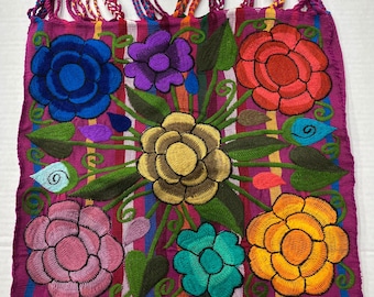 May include: A colorful embroidered tote bag with a pink background and a floral design. The bag has a striped pattern and a pink handle.