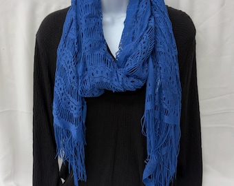 May include: A vibrant blue scarf featuring an intricate open-knit lace pattern and long fringe detailing at the ends. The scarf is draped around a white mannequin form, showcasing the textured fabric and the consistent deep blue color throughout.