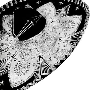 May include: A black sombrero with elaborate silver embroidery and embellishments. The hat features a wide brim and a black velvet crown. The silver detailing includes intricate patterns and decorative trim, creating a festive and elegant appearance.