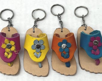 May include: Four leather sandal keychains in pink, yellow, orange, and blue, each with a flower accent. The keychains have silver-colored rings and chains, and the sandals are approximately 3 inches long.