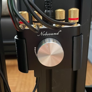 Könnte beinhalten: Ein schwarzer Audioverstärker mit einem silbernen Lautstärkeregler und vergoldeten Lautsprecheranschlüssen. Der Verstärker ist mit "Nobsound" beschriftet.