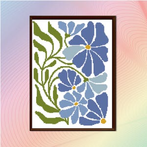 May include: A framed cross-stitch floral design featuring stylized blue flowers with yellow centers and green leaves. The artwork is set against a white background and framed in a dark brown wooden frame. The design has a vintage, handcrafted aesthetic.