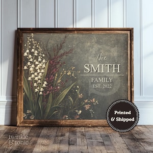 Puede incluir: Una impresión de arte mural rectangular en un marco de madera oscura con una ilustración botánica de lirios de los valles blancos y follaje oscuro sobre un fondo gris texturizado. El texto dice: the SMITH FAMILY EST. 2022. Una insignia circular dice Printed & Shipped.