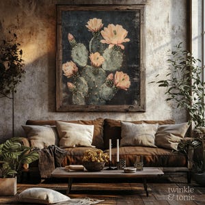 May include: A framed botanical print featuring a cactus with peach-colored flowers. The artwork hangs above a brown leather sofa with beige pillows. The room has a rustic, bohemian aesthetic with wooden furniture and plants.