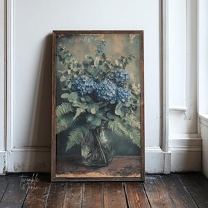 Pode incluir: Impressão emoldurada com uma natureza morta floral com hortênsias azuis e folhagem verde em um vaso de vidro transparente. A obra de arte tem uma estética vintage, com uma moldura de madeira escura e um fundo envelhecido. O texto "twinkle & tonic" está no canto inferior esquerdo.