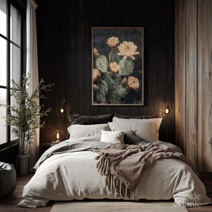 May include: A bedroom scene featuring a bed with light-colored bedding, a fringed throw blanket, and decorative pillows. A framed cactus print hangs above the bed. The room has dark wood paneling and a large window with a plant.