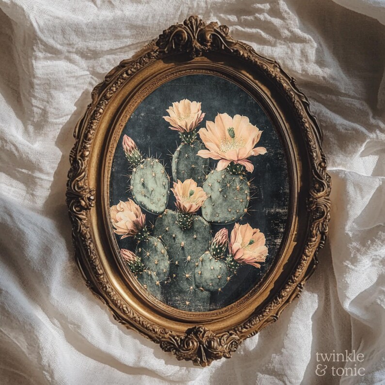 May include: An oval-shaped, antique gold frame surrounds a botanical print of a cactus with peach-colored flowers. The artwork features a dark background and the text "twinkle & tonic" in the lower right corner.