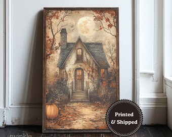 May include: A framed print of a cottage scene at night, with a full moon in the sky. The artwork features a house with a stone facade, a chimney, and a front door. A pumpkin sits in the foreground. The print is in a wooden frame.