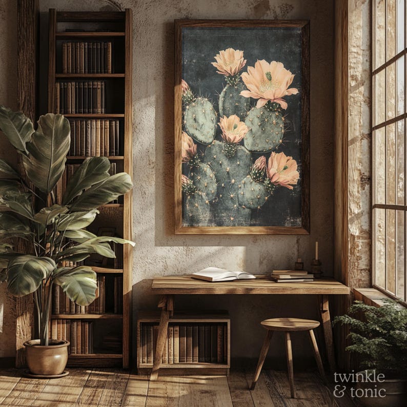 May include: A framed botanical print of a cactus with peach-colored flowers hangs above a wooden desk. A wooden bookshelf and a potted plant are on the left. A small wooden stool and a window are on the right. The image has a warm, rustic aesthetic.
