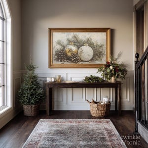 Op de afbeelding: Een warm verlichte entree met een ingelijst schilderij met kerstthema boven een donkere houten tafel. Links staat een kleine kerstboom in een gevlochten mand, met een gevlochten mand en een vloerkleed op de vloer.