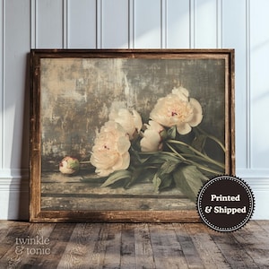 May include: A framed print featuring a still life of peonies. The flowers are a soft peach color with green leaves, set against a rustic, textured background. The wooden frame adds a vintage touch. The print is labeled "Printed & Shipped".