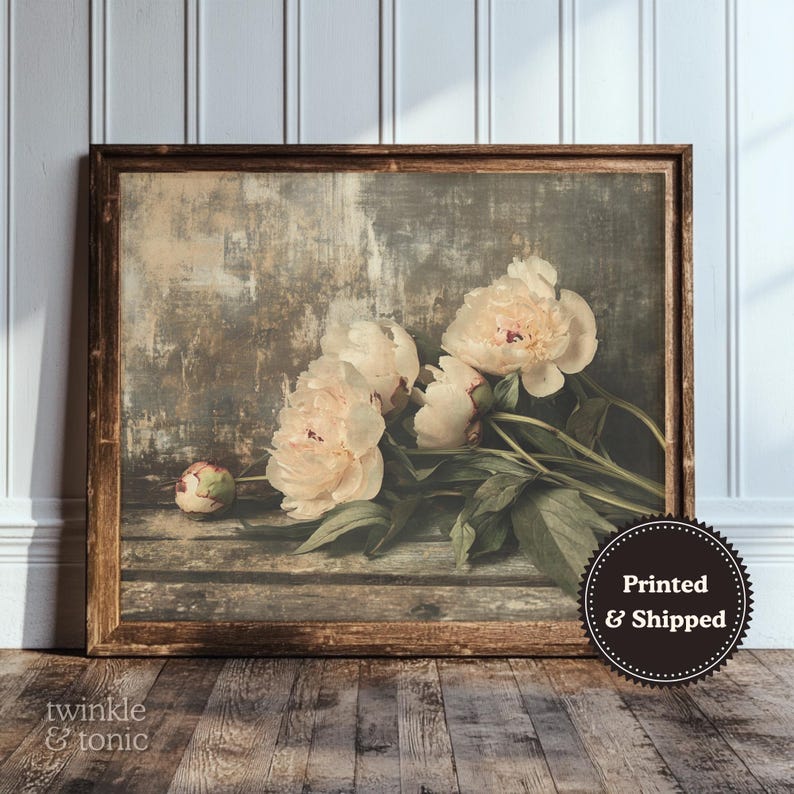 May include: A framed print featuring a still life of peonies. The flowers are a soft peach color with green leaves, set against a rustic, textured background. The wooden frame adds a vintage touch. The print is labeled "Printed & Shipped".