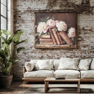 May include: A framed floral still life painting featuring pink and white peonies and antique books. The artwork hangs on a brick wall above a light-colored sofa with white pillows. A wooden coffee table and potted plant are in the foreground.