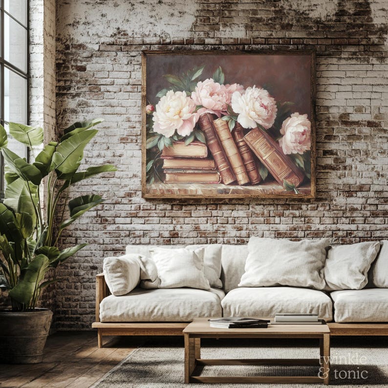 May include: A framed floral still life painting featuring pink and white peonies and antique books. The artwork hangs on a brick wall above a light-colored sofa with white pillows. A wooden coffee table and potted plant are in the foreground.