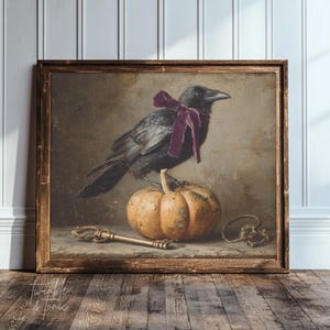 May include: A framed vintage-style painting featuring a black crow perched on an orange pumpkin. The crow wears a purple bow. A gold key and decorative element are at the base of the pumpkin. The artwork has a rustic, antique aesthetic.