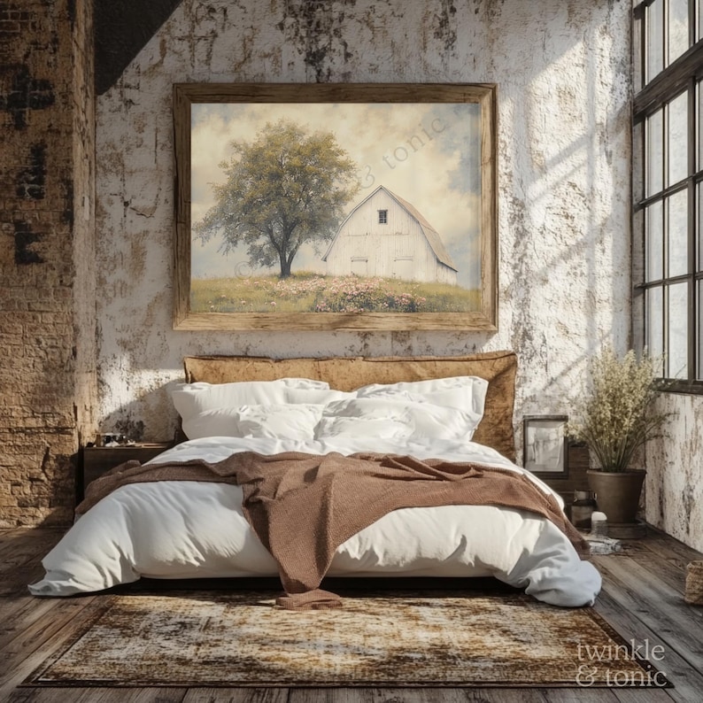 Op de afbeelding: Een slaapkamer met een ingelijst landschapsschilderij van een witte schuur en een boom. Het bed heeft wit beddengoed, een bruine sprei en een patroonkleed. De kamer heeft een rustieke, vintage esthetiek met baksteen en een groot raam.