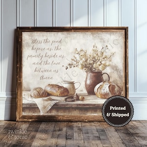 Puede incluir: Impresión enmarcada que presenta una naturaleza muerta con pan, flores y una jarra de cerámica. La obra de arte incluye el texto "Bless the food before us, the family beside us, and the love between us, Amen". La impresión tiene una estética rústica.
