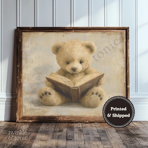 May include: A framed print featuring a tan teddy bear reading a brown book. The bear is centered, with a vintage-style background. The frame is brown, and the print has the text "twinkle & tonic" in the bottom left corner.