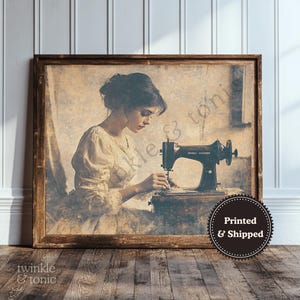 May include: A sepia-toned framed print shows a woman using a black antique sewing machine. She wears a cream-coloured dress. The frame is dark brown. The words "twinkle & tonic" are in the bottom left corner. The image has a vintage aesthetic.